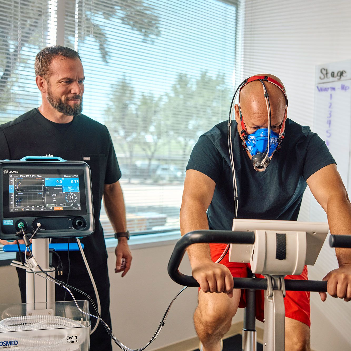 A man performing a VO2 max test on a stationary bike while a Preamble clinician monitors his results