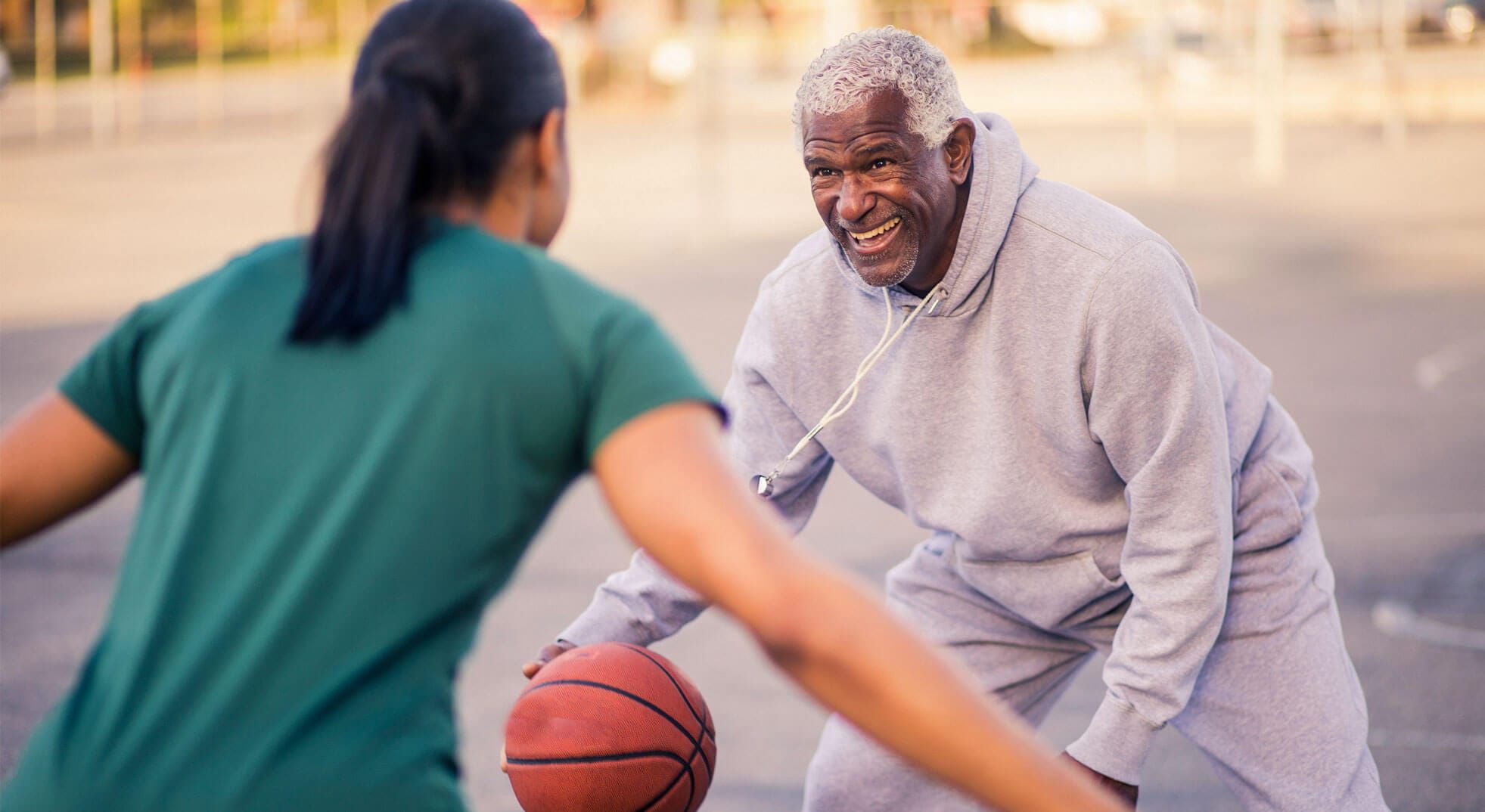 Smiling older man playing one-on-one basketball outdoors with a younger woman