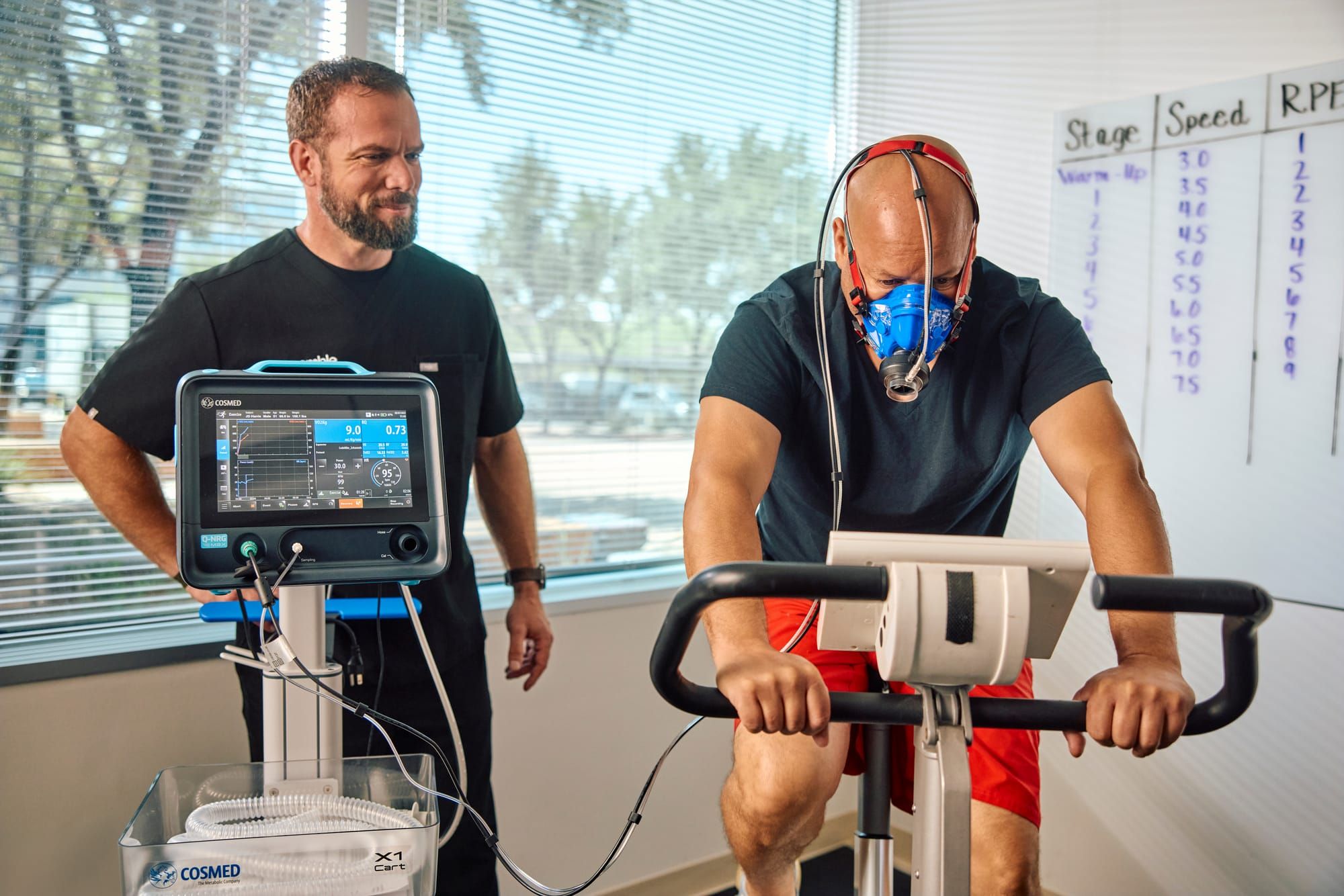 Man performing a VO2 max test on a stationary bike while a Preamble clinician monitors the metabolic cart