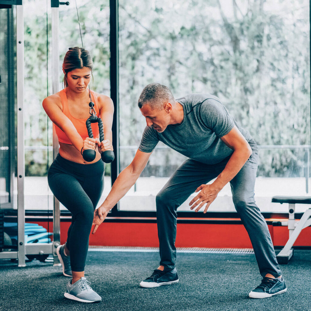 Personal trainer guiding a woman through strength training in a gym.