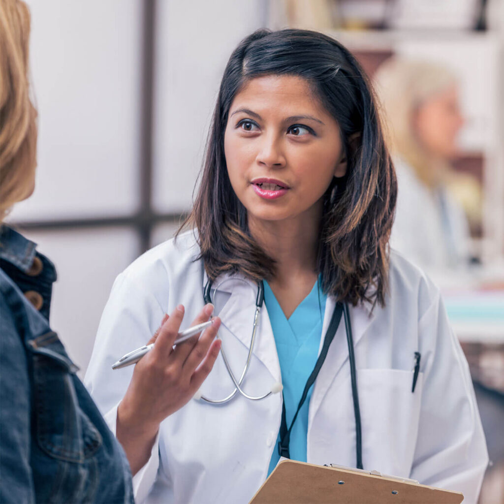 Female doctor speaking with a patient while holding a clipboard.
