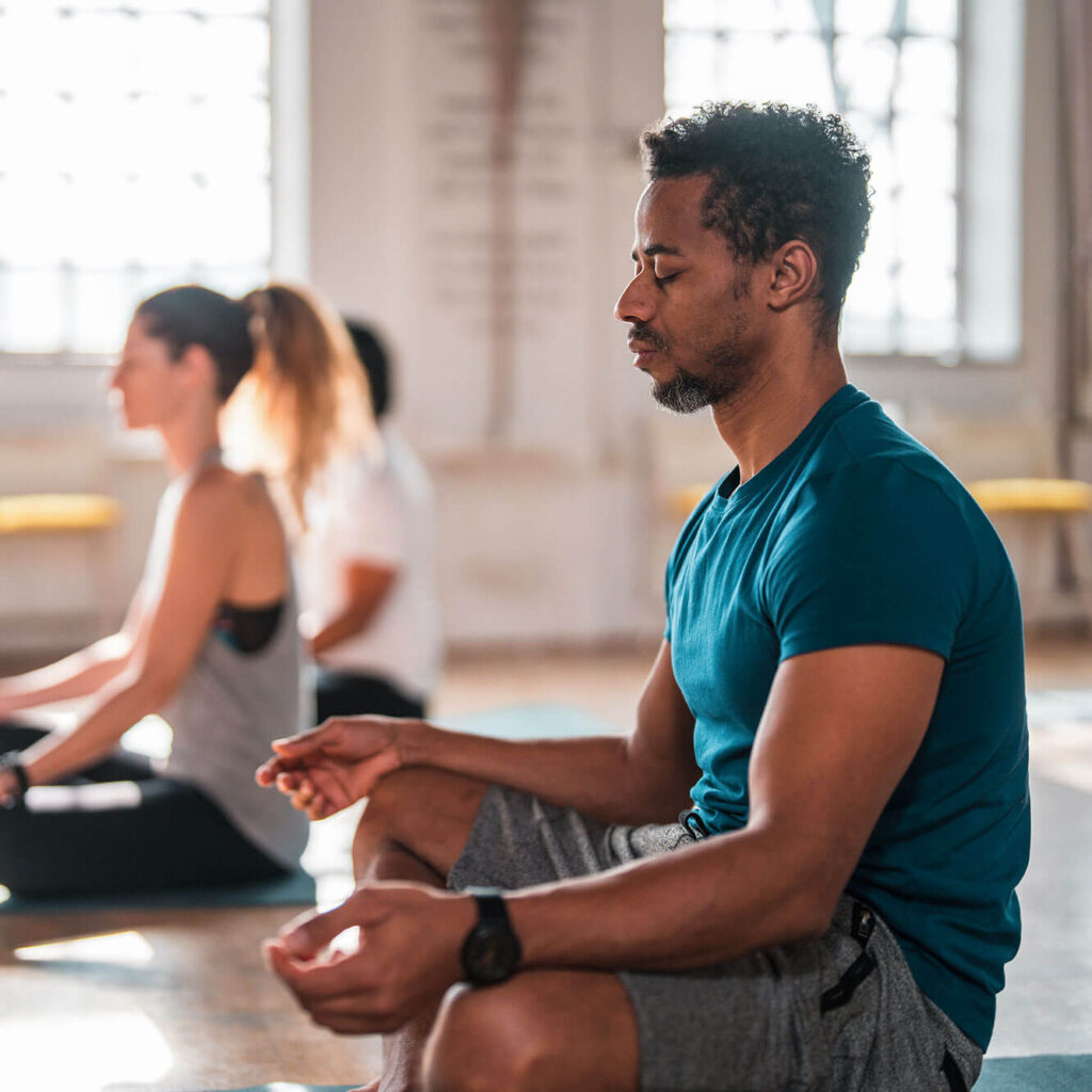 Man meditating in a group yoga class focused on wellness.